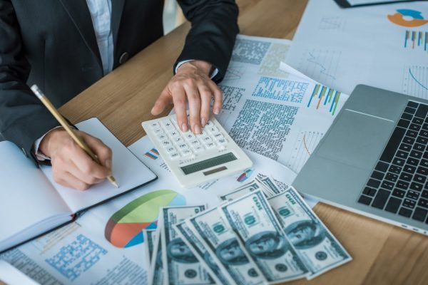 cropped image of financier using calculator and writing something to notebook in office